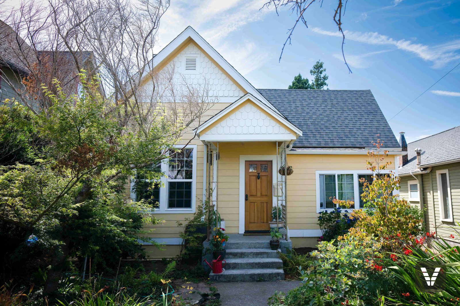 Completed butter-yellow James Hardie re-side with white scalloped gables and a craftsman wood door on a Bellingham cottage