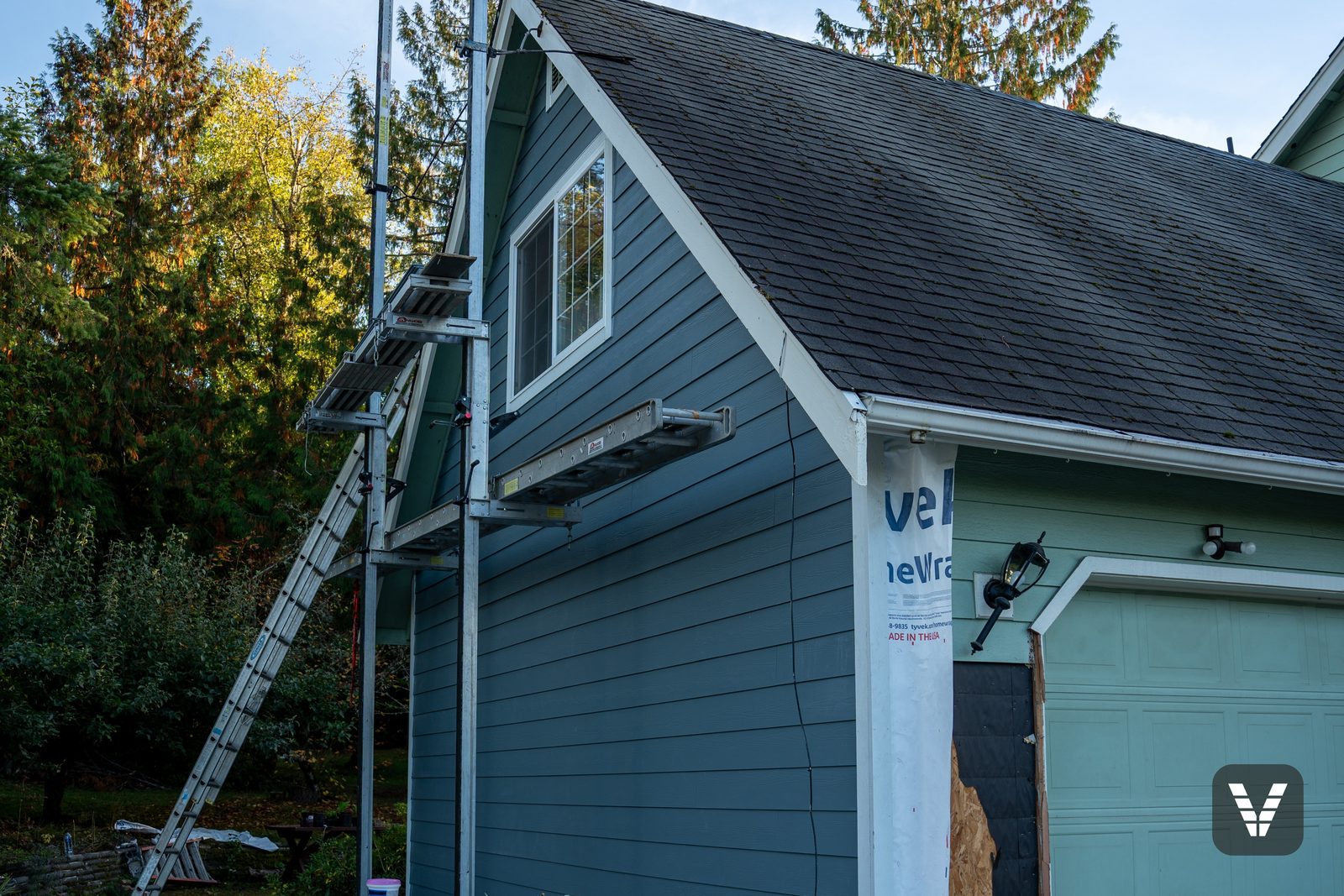 Fiber cement lap going up a Bellingham gable from pump-jack scaffolding, the housewrap still showing at the corner