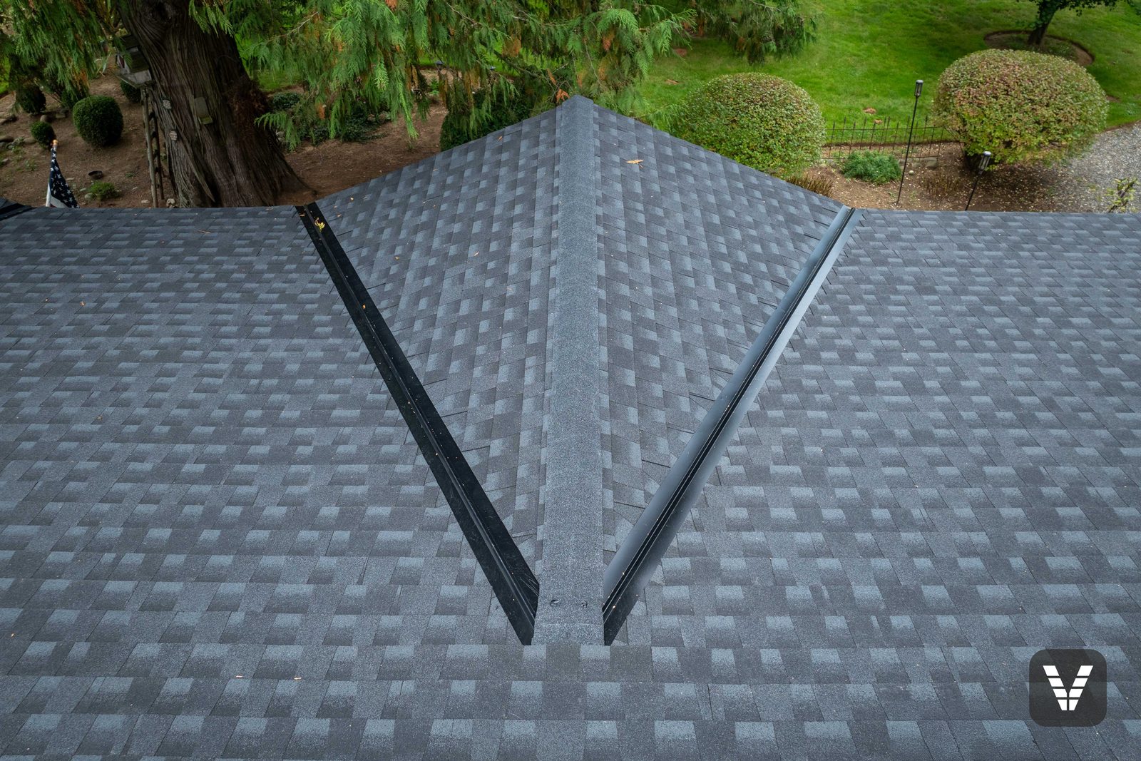 Where two valleys meet at the dormer — black metal flashing lines and the TimberCrest ridge cap dead center — Siding & Window Vault project in Lynden, WA