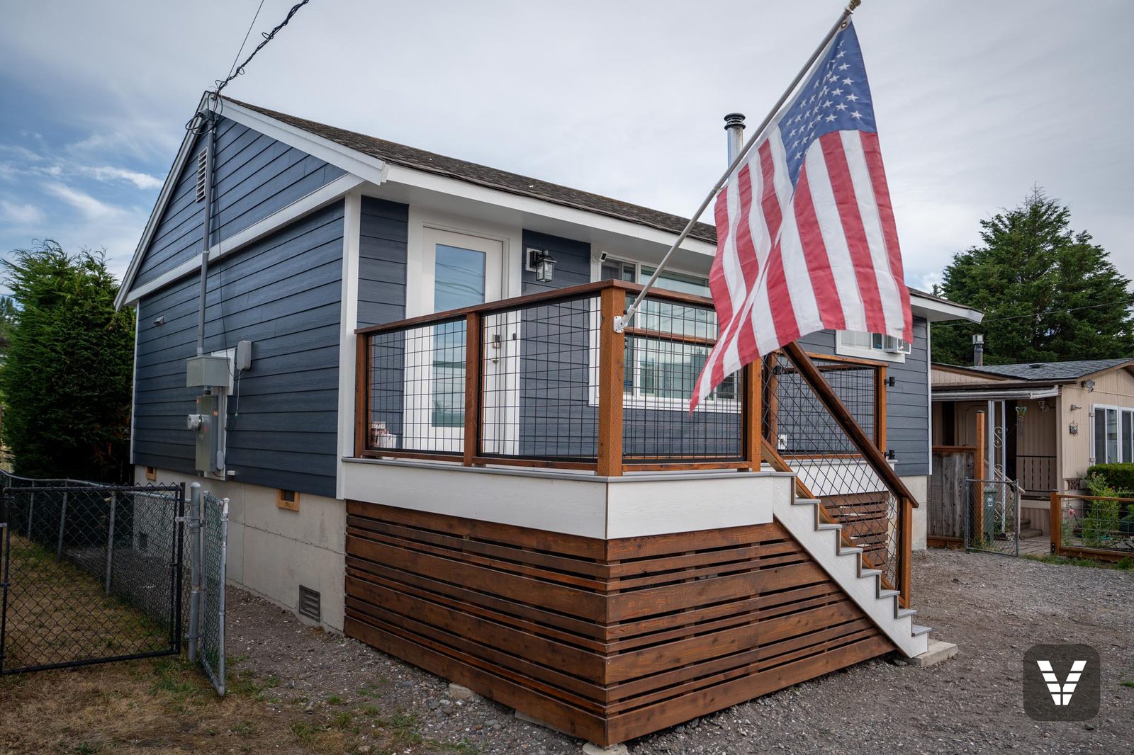 The finished deck corner — Deep Ocean lap, Arctic White skirt, cedar rails, and the flag flying