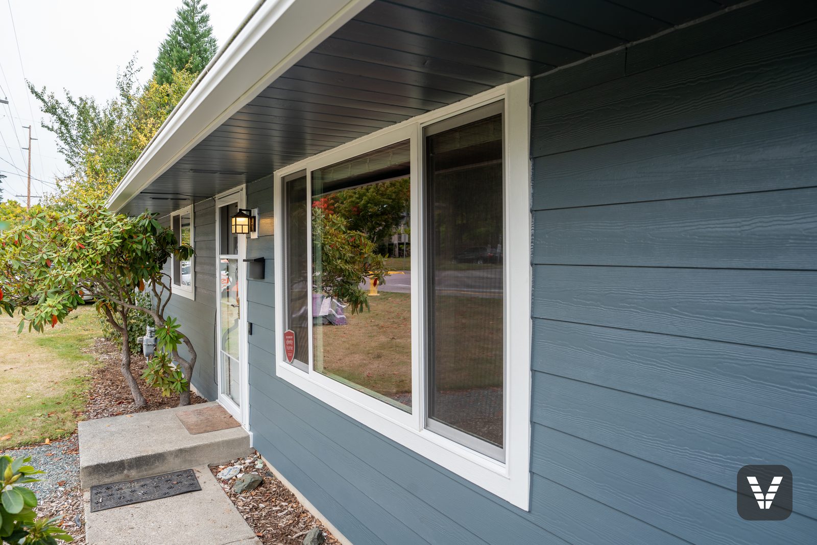 A new three-panel Milgard V400 Tuscany window beside the entry of an Anacortes home, installed full-frame and trimmed in Arctic White HardieTrim
