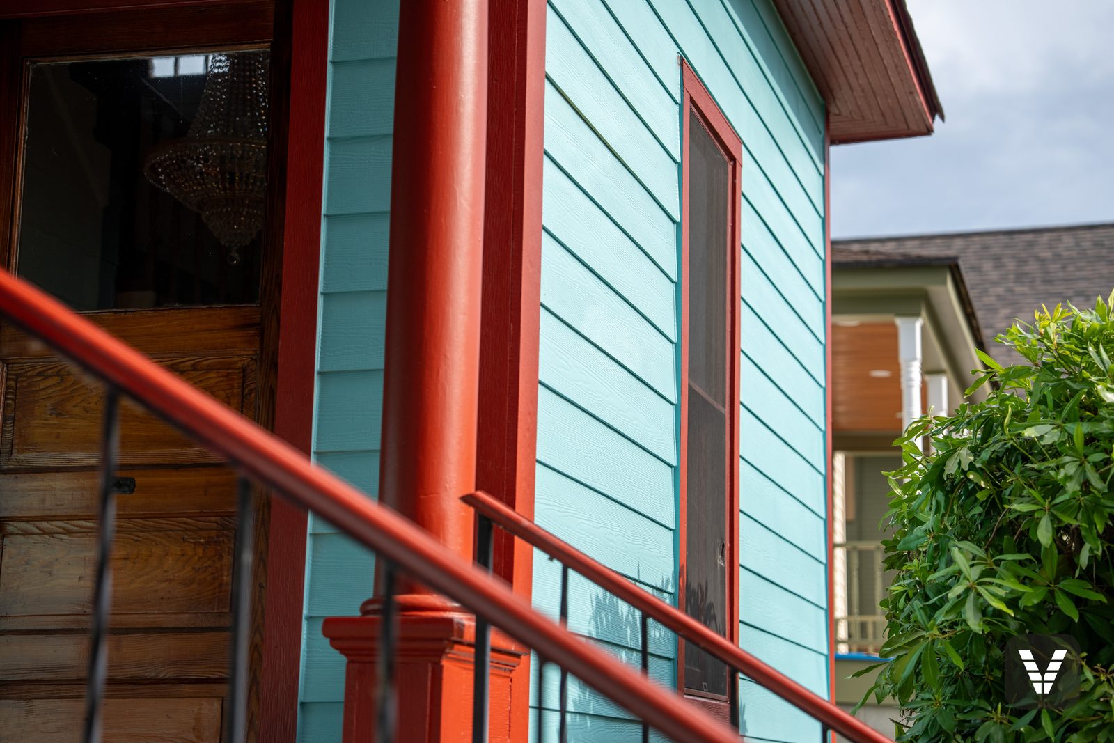 The porch — original stained-wood front door and iron railings against new turquoise HardiePlank